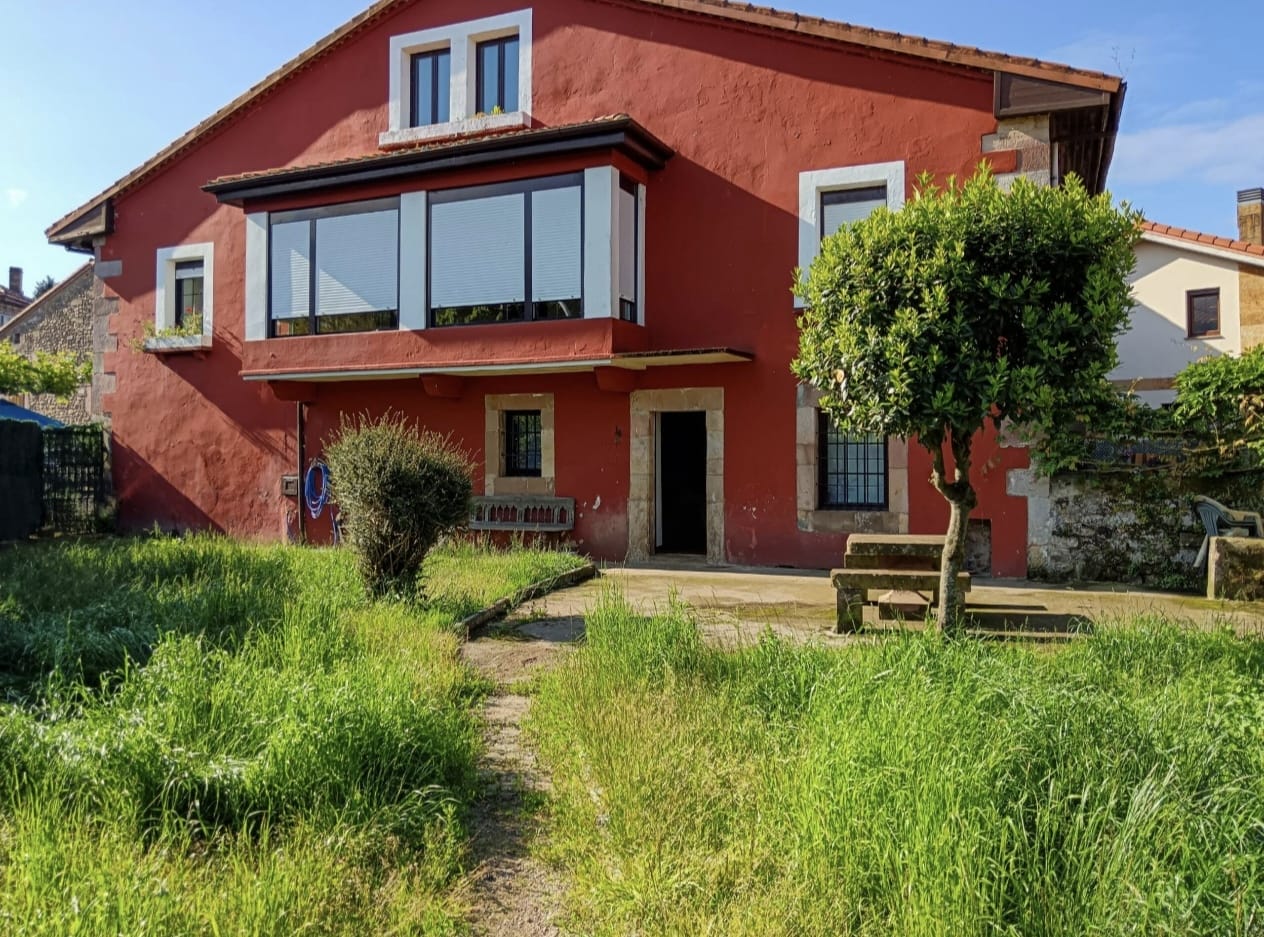 Casa rural con jardín y fachada roja en entorno natural de Cantabria